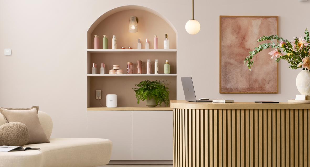 Eero Wi-Fi device placed on a shelf in a stylish reception or workspace with decorative bottles, plants, and a laptop on a wooden counter.